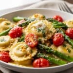 Ravioli with tomatoes and asparagus in olive oil with garlic and herbs, Parmesan garnish