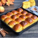 Torn pumpkin yeast roll showing tender crumb, brushed with butter and honey.​