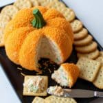Spreading Pumpkin Cheese Ball on whole wheat crackers; creamy cheddar texture.