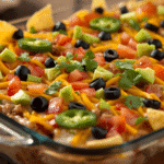 V4: Alt: Seven layer bean dip topped with cheddar, tomatoes, olives, and scallions over guacamole, sour cream, and refried beans.