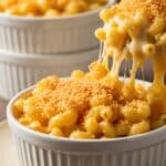 Serving spoon lifting extra creamy mac and cheese with golden crust.