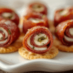Close-up Salami Roll Ups with cream cheese, chives, and toothpicks on white platter.​