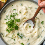 Alt Text: Spoon lifting cheesy Homemade Alfredo from a rustic skillet.