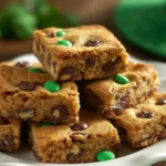 A child reaching for a St. Patrick’s Day Chocolate Chip Cookie Bar on a plate.